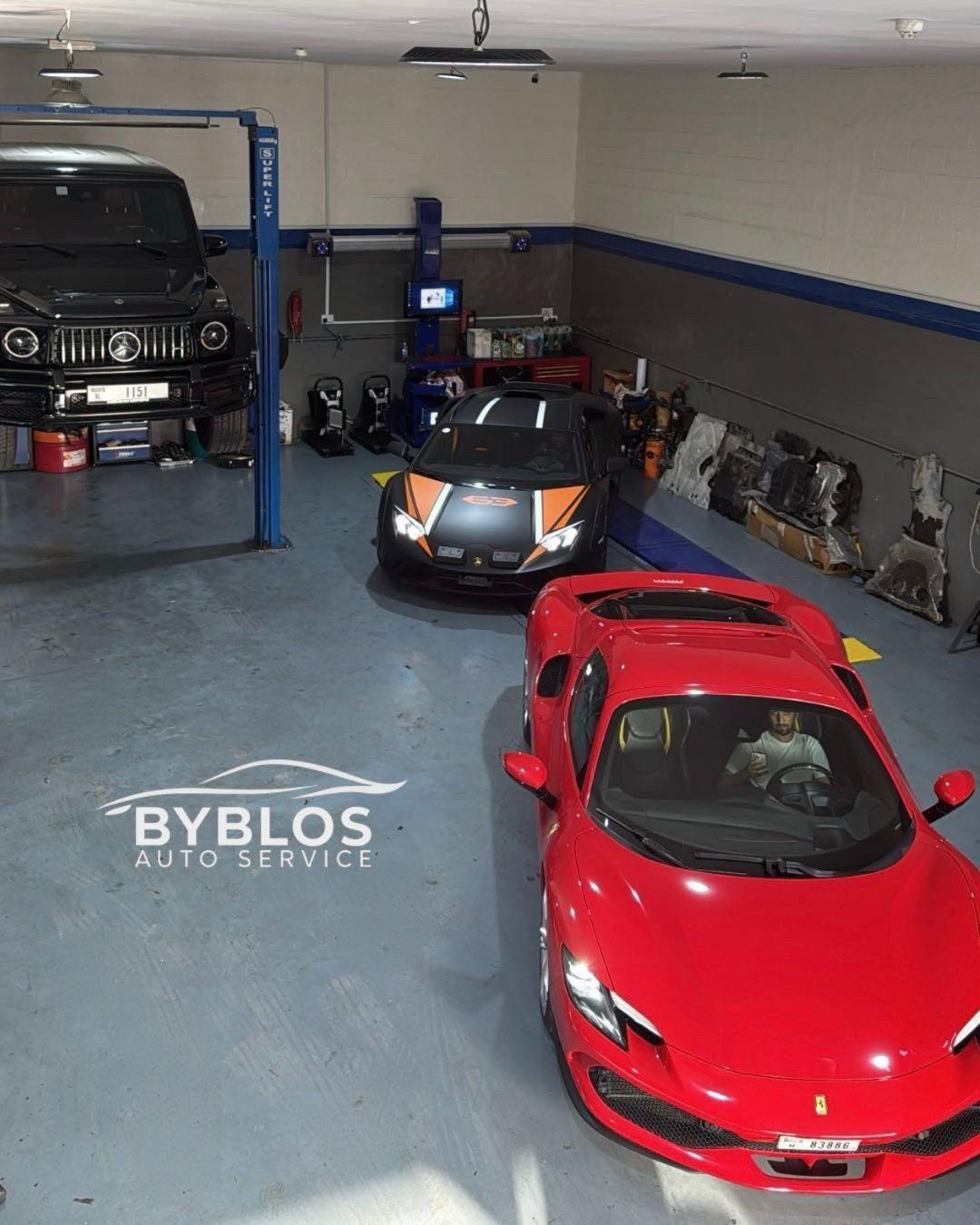 A red Ferrari, a Lamborghini and a black G-Class inside the workshop, lifts behind them